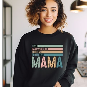 May include: Black sweatshirt with a retro-style graphic that reads "Loved, Hardworking, Selfless, Protective, Mama" in colorful stripes.