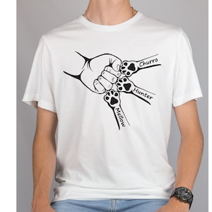 May include: White t-shirt with a black graphic of four paw prints holding hands. The paw prints are labeled "Mellow", "Hunter", "Churro", and "Churro".