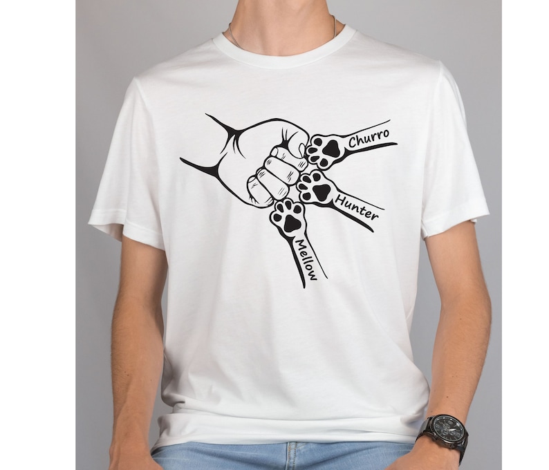 May include: White t-shirt with a black graphic of four paw prints holding hands. The paw prints are labeled "Mellow", "Hunter", "Churro", and "Churro".