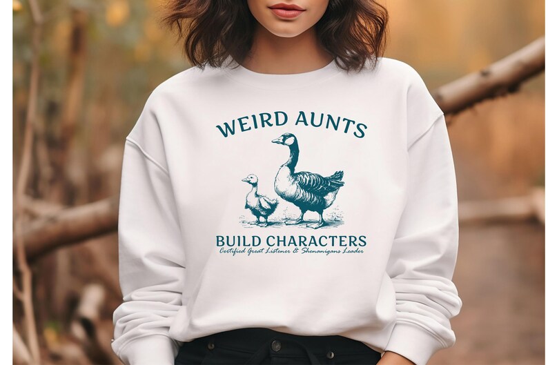 May include: White sweatshirt with the text "WEIRD AUNTS BUILD CHARACTERS" in teal. The graphic features a goose and a gosling. The sweatshirt also has the text "Certified Great Listener & Shenanigans Leader".