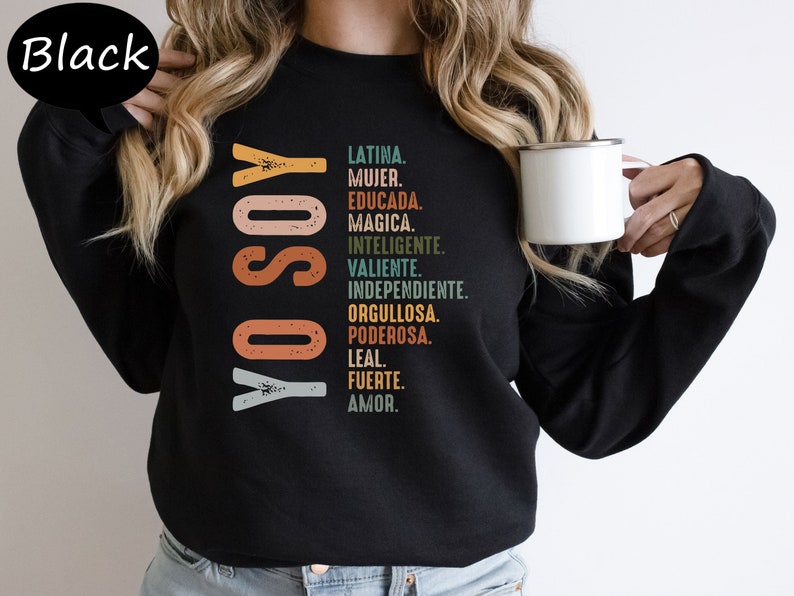 K&ouml;nnte beinhalten: Schwarzes Sweatshirt mit dem Text "YO SOY" in einer bunten Retro-Schrift und einer Liste spanischer W&ouml;rter, die die Eigenschaften einer Frau beschreiben.