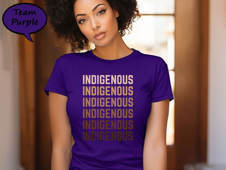 Pu&ograve; includere: Una maglietta viola con la parola "INDIGENOUS" stampata pi&ugrave; volte in un gradiente di colore oro. La frase "Team Purple" &egrave; in un fumetto viola in alto a sinistra. La maglietta &egrave; a maniche corte.