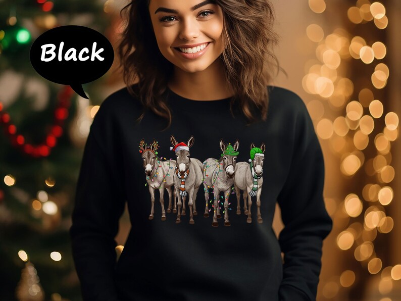 May include: Black sweatshirt with a Christmas-themed design of four donkeys. Each donkey is decorated with festive hats, scarves, and fairy lights. The word "Black" is in a speech bubble.