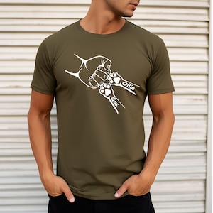 May include: A green t-shirt with a white design of a hand and two paw prints. The paw prints have the names "Gus" and "Ollie" written next to them.