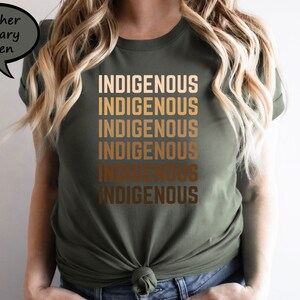 Pu&ograve; includere: T-shirt verde militare melange con la parola "INDIGENOUS" stampata in una sfumatura di toni oro. La t-shirt, a girocollo, &egrave; annodata in vita. La maglietta &egrave; realizzata in un materiale morbido.