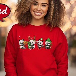 May include: Red Christmas sweatshirt featuring four adorable pandas wearing Santa hats and holding Christmas decorations. The pandas are surrounded by Christmas lights and a Christmas tree.