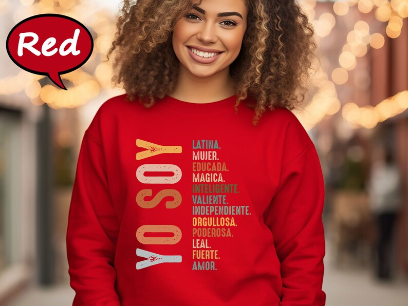 K&ouml;nnte beinhalten: Roter Pullover mit dem Text "YO SOY" in einer vertikalen, bunten Retro-Schrift. Dem Text folgt eine Liste spanischer W&ouml;rter, die die Eigenschaften einer Frau beschreiben, darunter Latina, Mujer, Educada, Magica, Inteligente, Valiente, Independiente, Orgullosa, Poderosa, Leal, Fuerte, Amor.