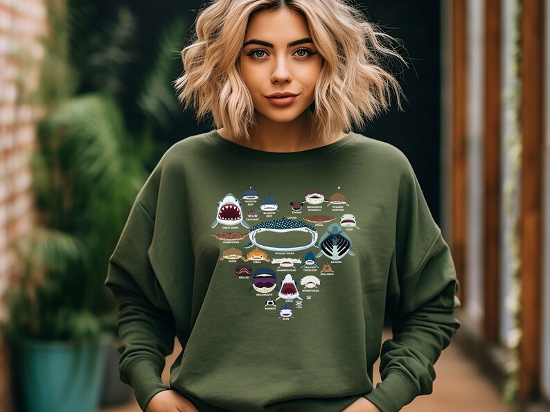 May include: A green sweatshirt with a heart-shaped design featuring various types of sharks. The design includes the names of each shark species.