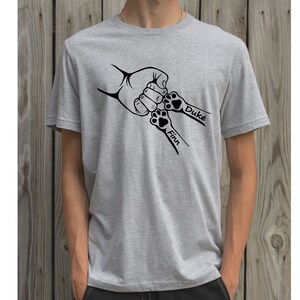 May include: A gray t-shirt with a black graphic of a hand and two paw prints. The paw prints have the names "Finn" and "Duke" written next to them.