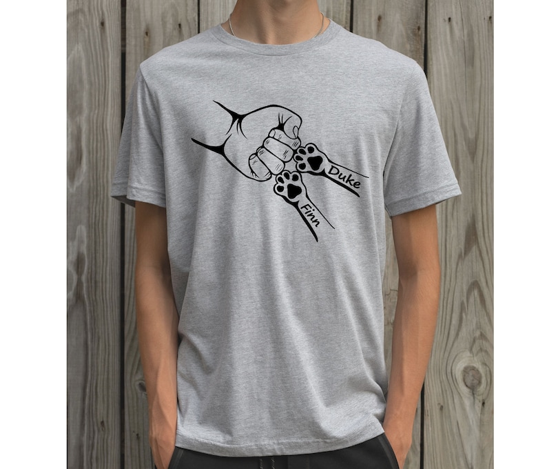 May include: A gray t-shirt with a black graphic of a hand and two paw prints. The paw prints have the names "Finn" and "Duke" written next to them.