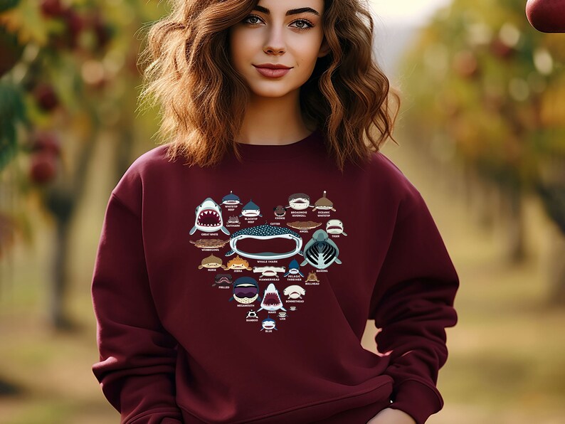 May include: A maroon sweatshirt with a heart-shaped design featuring various shark species. The design includes the names of each shark species.