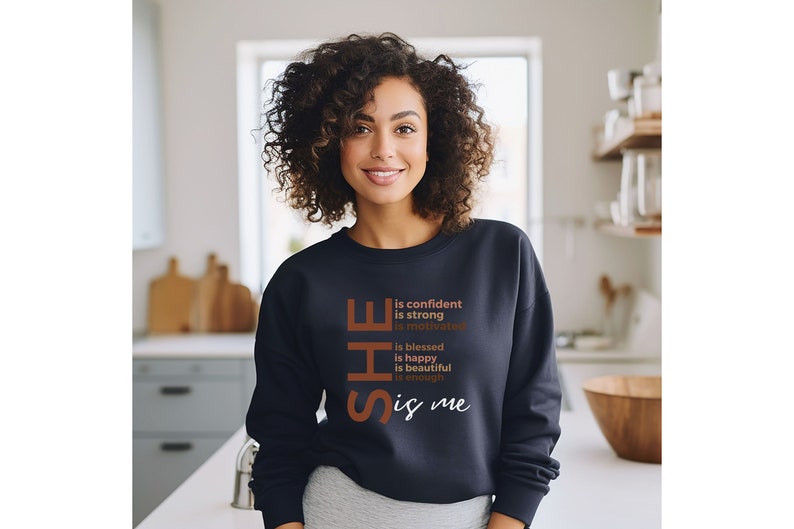Op de afbeelding: Een marineblauw sweatshirt met de tekst "SHE is confident is strong is motivated is blessed is happy is beautiful is enough is me" in bruin gedrukt op de voorkant.