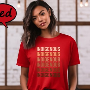 Pu&ograve; includere: Una maglietta rossa con la parola "INDIGENOUS" stampata pi&ugrave; volte in una sfumatura di colori oro. La maglietta &egrave; indossata da una persona. La parola "Red" &egrave; in un fumetto rosso in alto a sinistra.