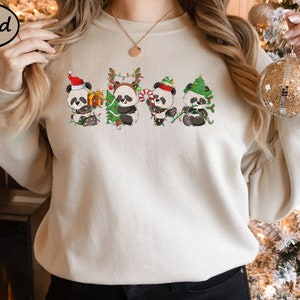 May include: A cream-coloured sweatshirt featuring a graphic of five pandas wearing Santa hats and holding Christmas trees. The pandas are wearing red, green and white.