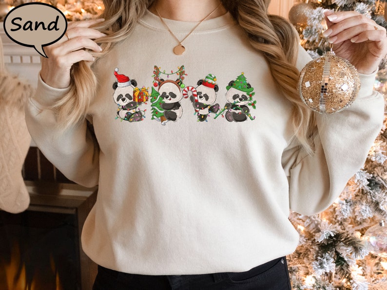 May include: A cream-coloured sweatshirt featuring a graphic of five pandas wearing Santa hats and holding Christmas trees. The pandas are wearing red, green and white.