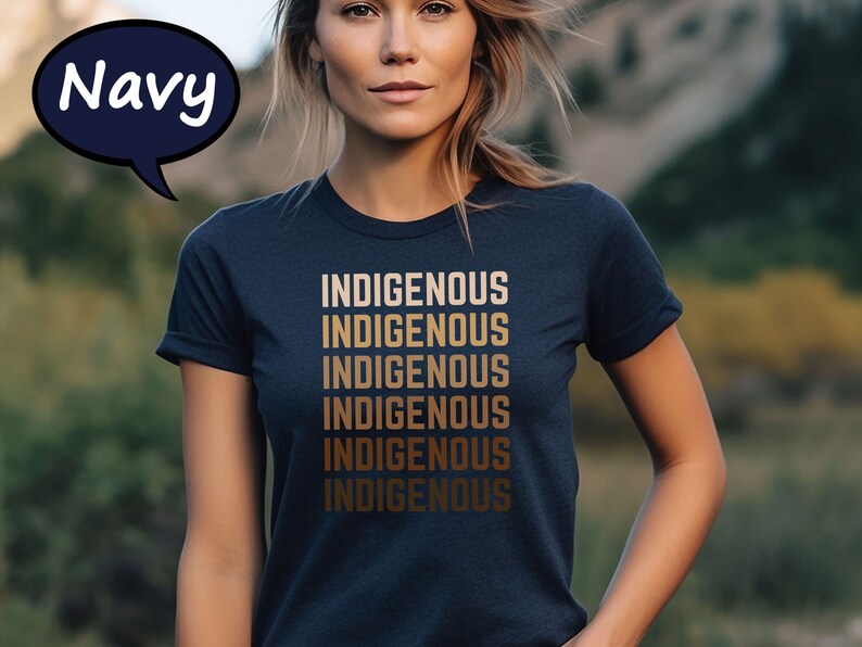 Pu&ograve; includere: T-shirt blu navy con la parola "INDIGENOUS" stampata in una sfumatura di toni oro, ripetuta sei volte. La maglietta &egrave; a girocollo. Una nuvoletta blu navy con la parola "Navy" si trova nell'angolo in alto a sinistra.