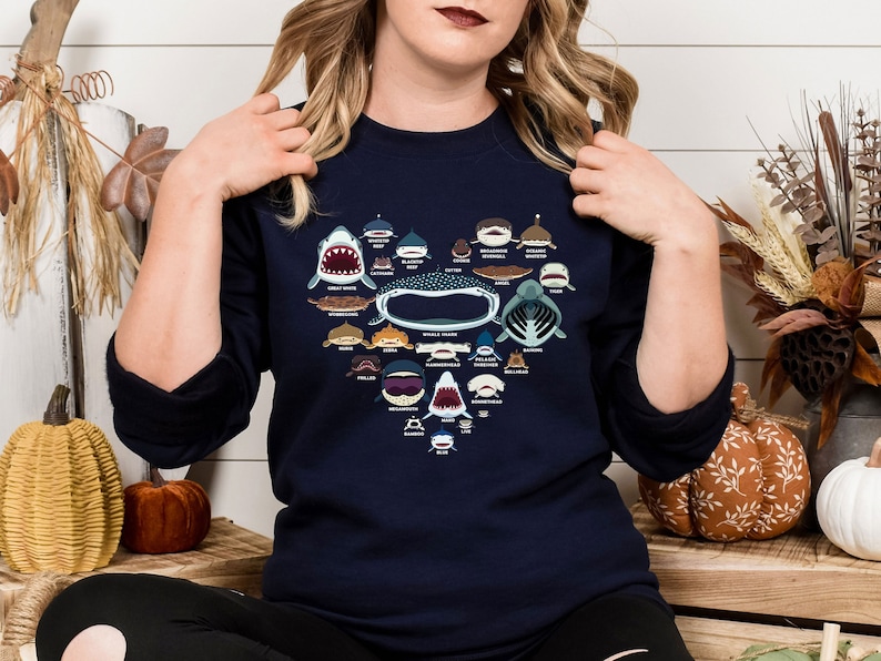 May include: A navy blue sweatshirt with a heart-shaped design featuring illustrations of different types of sharks. The design includes the names of each shark species.