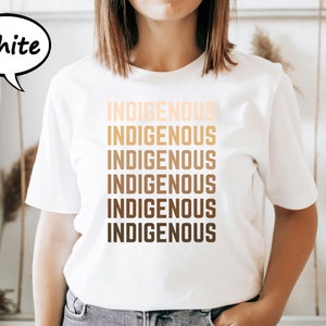 Pu&ograve; includere: T-shirt bianca con la scritta "INDIGENOUS" stampata in un gradiente di tonalit&agrave; marroni. La parola &egrave; ripetuta verticalmente sei volte. Una nuvoletta con la parola "White" si trova nell'angolo in alto a sinistra.