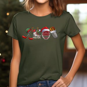 May include: A green t-shirt with a Christmas-themed hockey design. The design features a hockey stick, skates, a hockey helmet, and a Santa hat.