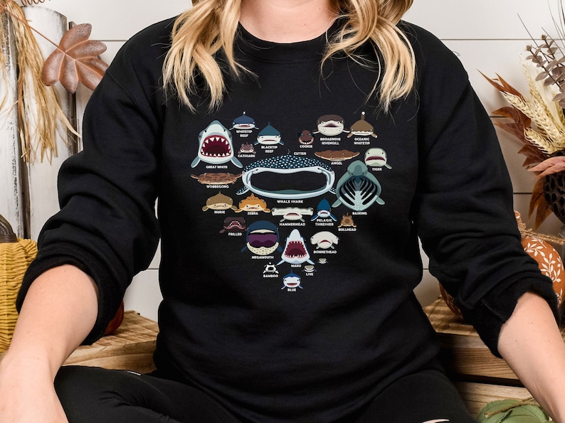 May include: Black sweatshirt with a heart-shaped design featuring illustrations of different types of sharks and their names. The names include Great White, Wobbegong, Hammerhead, and more.