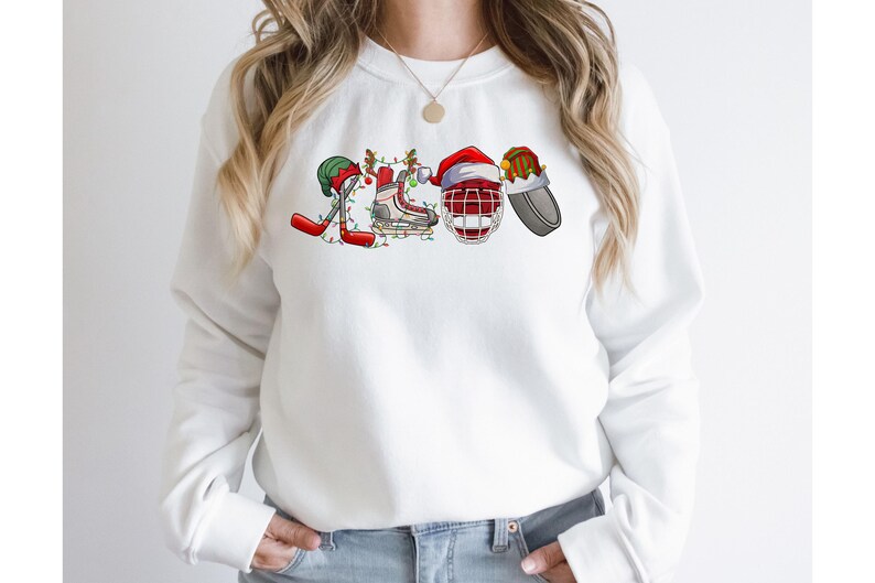 May include: White sweatshirt with a Christmas-themed hockey design. The design features a hockey stick, a hockey skate, a hockey helmet, and a puck, all decorated with Christmas lights and ornaments.