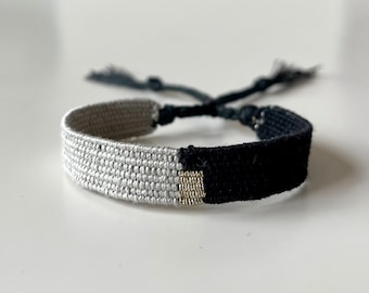 Könnte beinhalten: Ein geflochtenes Freundschaftsarmband in Schwarz und Weiß mit einem goldenen Akzent. Das Armband ist an einem Ende mit einem Knoten gebunden.