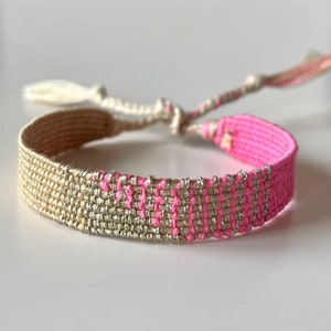 Può includere: Un braccialetto di amicizia intrecciato con un design rosa e oro. Il braccialetto ha un fiocco ad ogni estremità.