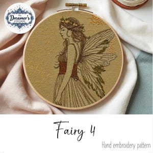 May include: Hand-embroidered artwork in a wooden hoop. The design features a fairy with detailed wings, a floral crown, and a flowing dress. The text "Fairy 4" and "Hand embroidery pattern" are displayed below the artwork. The Dreamer's Stitchery logo is in the upper left.