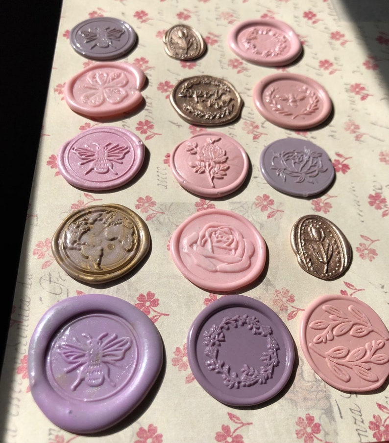 May include: Assortment of wax seals in various colors and designs, including bees, flowers, and wreaths. The seals are arranged on a patterned surface.