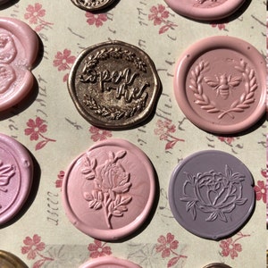 May include: Assortment of wax seals with various designs, including floral, bee, and tulip motifs. The seals are in shades of pink, purple, and gold.