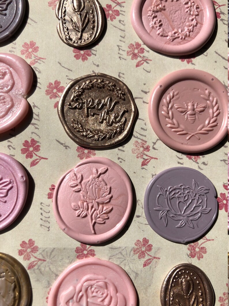 May include: Assortment of wax seals with various designs, including floral, bee, and tulip motifs. The seals are in shades of pink, purple, and gold.