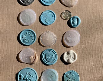 May include: A collection of decorative wax seals in various colors and designs. The seals feature floral, butterfly, and fruit motifs. Some seals are light blue, others are white, and some are a pearlescent color.