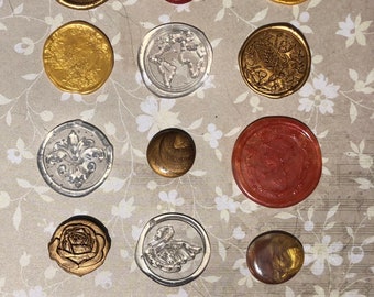 May include: Assortment of 15 wax seals with various designs, including a swan, a rose, a globe, a fleur-de-lis, and a butterfly. The seals are in gold, silver, red, and clear.