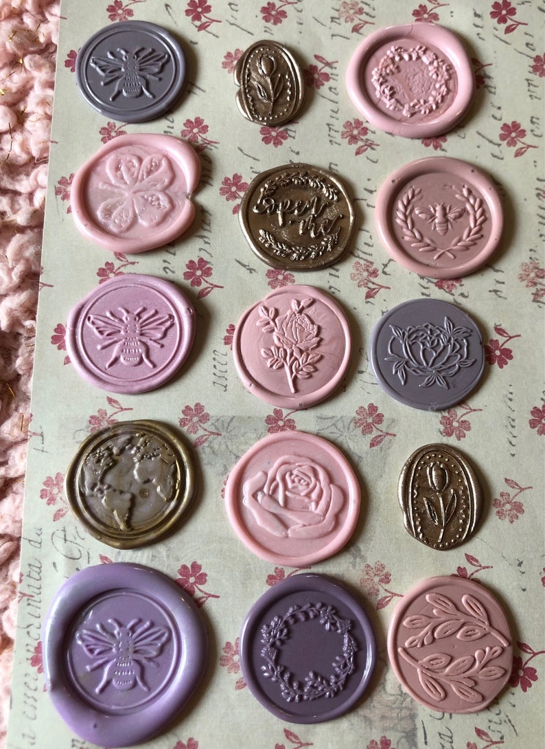 May include: Assortment of 13 wax seals with various designs, including bees, flowers, leaves, and a globe. The seals are in shades of pink, purple, and gold.