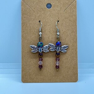 May include: A pair of silver dragonfly earrings with iridescent purple and green beads and pink crystal beads hanging from the dragonfly.