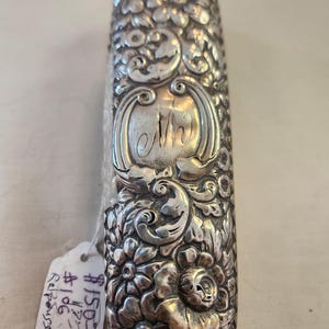 May include: A silver, ornate, rectangular box with a floral design and an engraved letter "M".