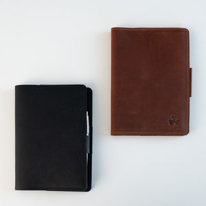 May include: Two leather-bound journals, one black and one brown. The brown journal has a small clover embossed on the front cover.