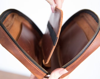 May include: A brown leather travel case with a zip closure and an interior pocket. The case is open and the interior is visible.