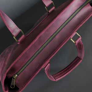 May include: A burgundy leather tote bag with a zipper closure and brass-colored hardware. The bag has two handles and a shoulder strap. The leather has a distressed finish, giving it a vintage look.