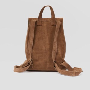 Puede incluir: Una mochila de ante marr&oacute;n con correas ajustables. La mochila tiene un cierre de solapa y un asa superior.