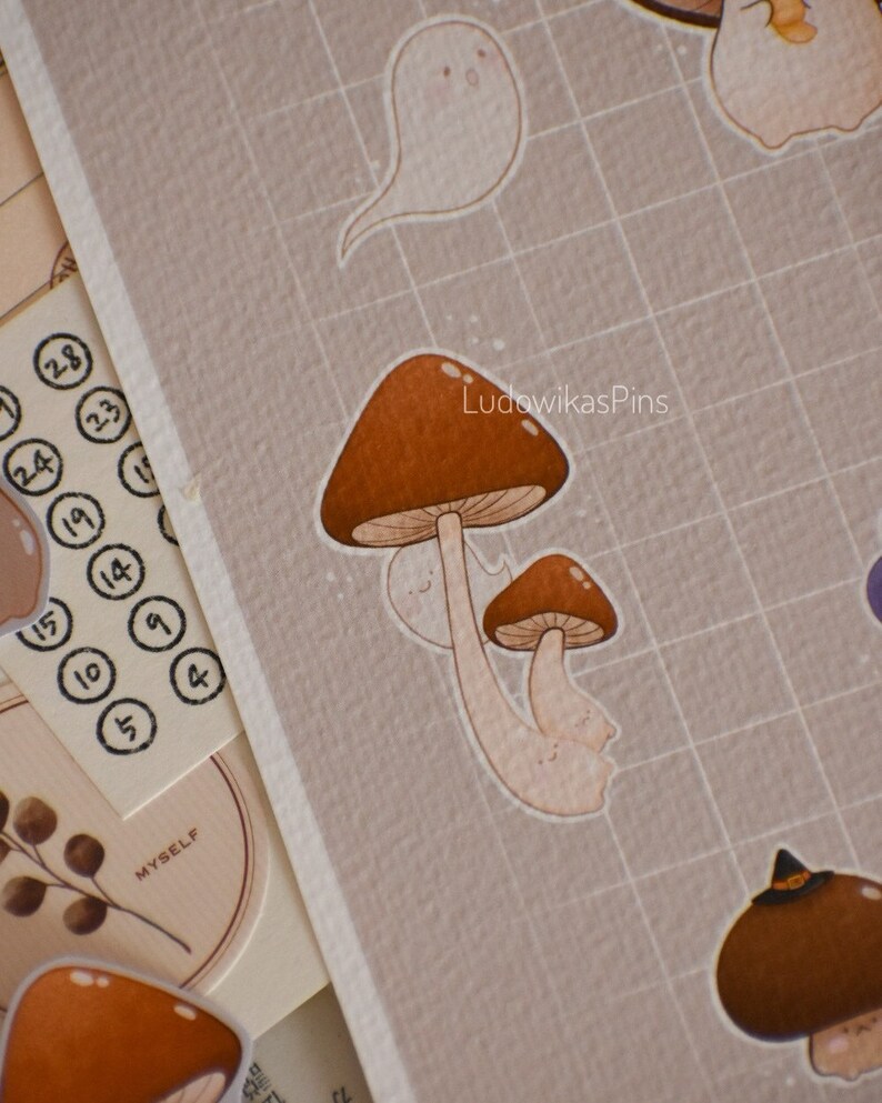 Puede incluir: Un conjunto de pegatinas de setas marrones y blancas con una pegatina de fantasma. Las pegatinas est&aacute;n sobre un fondo de cuadr&iacute;cula marr&oacute;n. El texto "LudowikasPins" est&aacute; en la esquina superior derecha de la imagen.