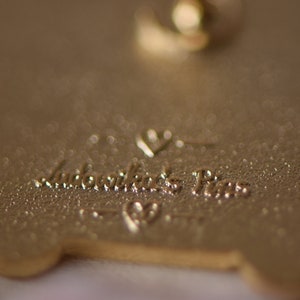 May include: Gold-colored metal pin with a heart and the text "Remarkable Pins" on the back.