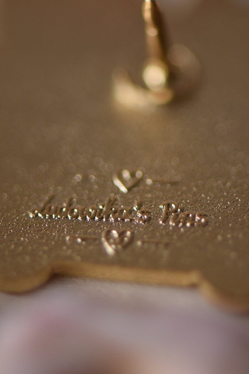 May include: Gold-colored metal pin with a heart and the text "Remarkable Pins" on the back.