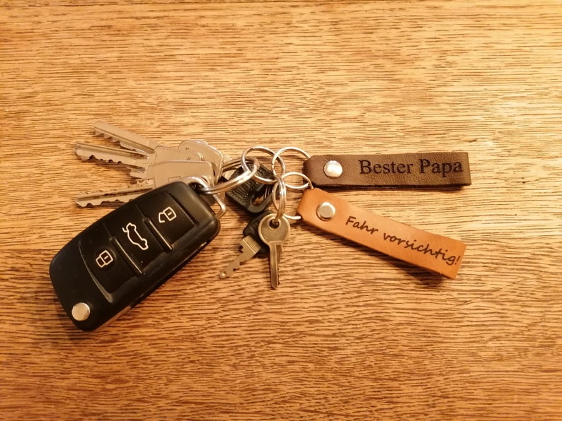 May include: A set of keys with a brown leather keychain that says "Bester Papa" and a tan leather keychain that says "Fahr vorsichtig!"