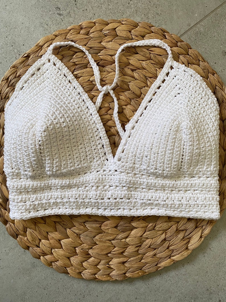 May include: White crocheted halter top with a deep V-neckline. The top is made with a simple stitch pattern and has a relaxed fit.