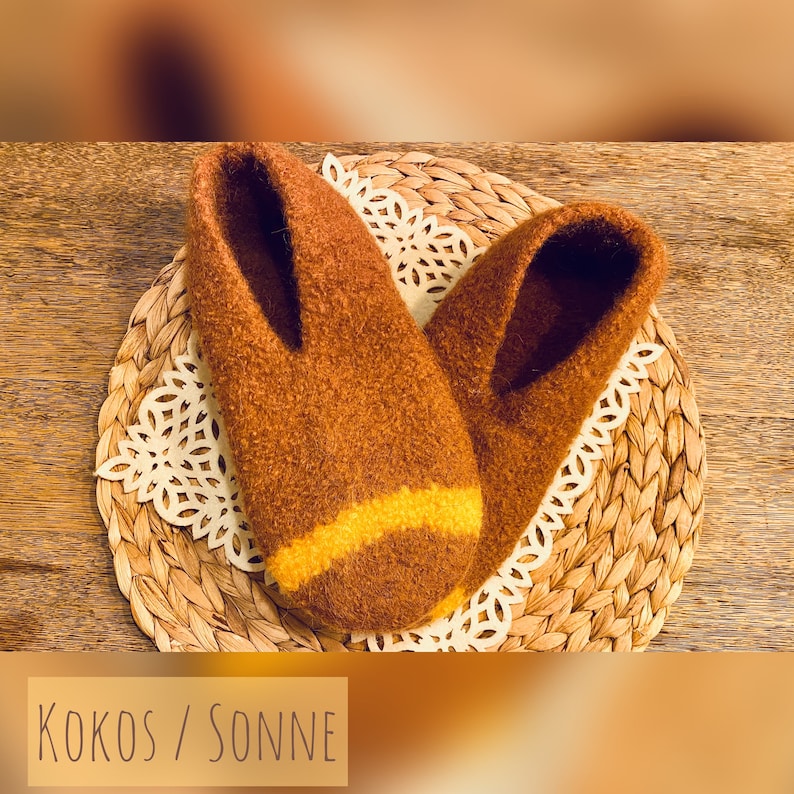 May include: A pair of brown fuzzy slippers with a yellow stripe across the top. The slippers are sitting on a woven straw mat.
