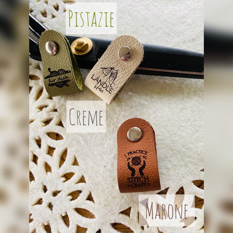 May include: Three leather needle protectors in pistachio green, cream, and brown, each with a silver snap closure. The green protector has the text "f&uuml;r dich", the cream one has "L&Auml;NDLE", and the brown one says "I PRACTICE STITCH CRAFT".