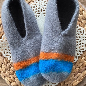May include: A pair of gray wool slippers with orange and blue stripes. The slippers are on a woven mat.