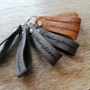 May include: Five brown leather keychains with silver key rings. Each keychain has the word "Lieblingssteam" engraved on it.