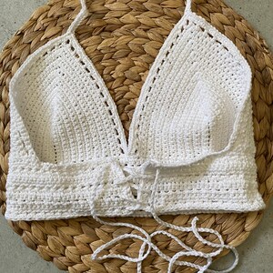 May include: White crocheted halter top with a lace-up front. The top is made with a delicate stitch and has a relaxed fit.